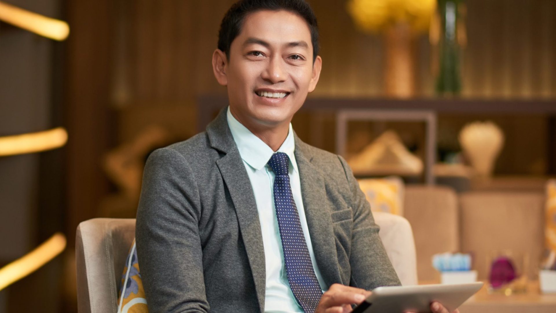 Portrait of happy Vietnamese entrepreneur sitting on chair in cafe